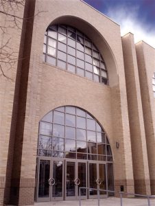 Main entrance to the Rochester School of the Arts with large glass windows over the door. The school is a beige brick building.